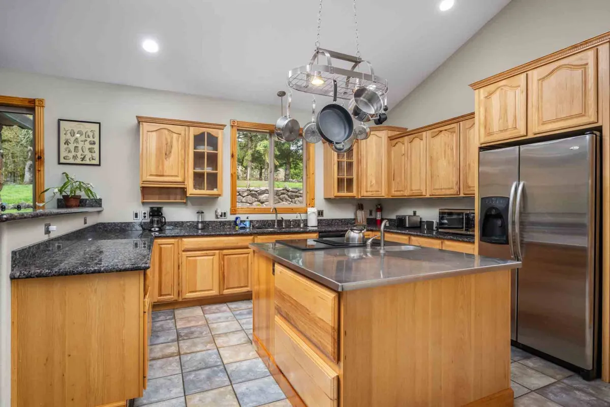 A bright, modern kitchen with a central island, stainless steel appliances, rich wooden cabinetry, and large windows that flood the space with natural light. The scene suggests a hub for cooking, gathering, and hosting, echoing the narrative’s focus on culinary experiences and wine pairing.