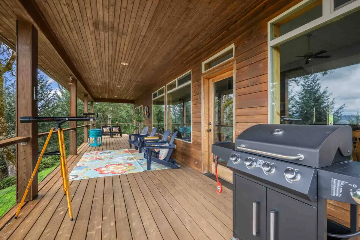 A cozy outdoor setup featuring a grill, a telescope positioned for stargazing, a cushioned seating area on a decorative rug, and views of the surrounding trees. The setting is casual, inviting, and ideal for both day and evening enjoyment, whether hosting a barbecue or gazing at the stars.