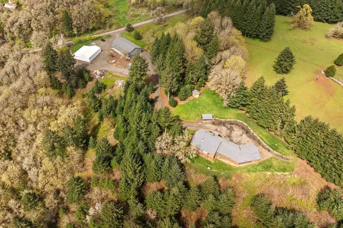 A broad exterior view showing the main house surrounded by wooded areas, outbuildings, and expanses of cleared land. The peaceful, expansive landscape underscores the property's secluded setting and natural beauty, providing a sense of privacy and space for group activities.