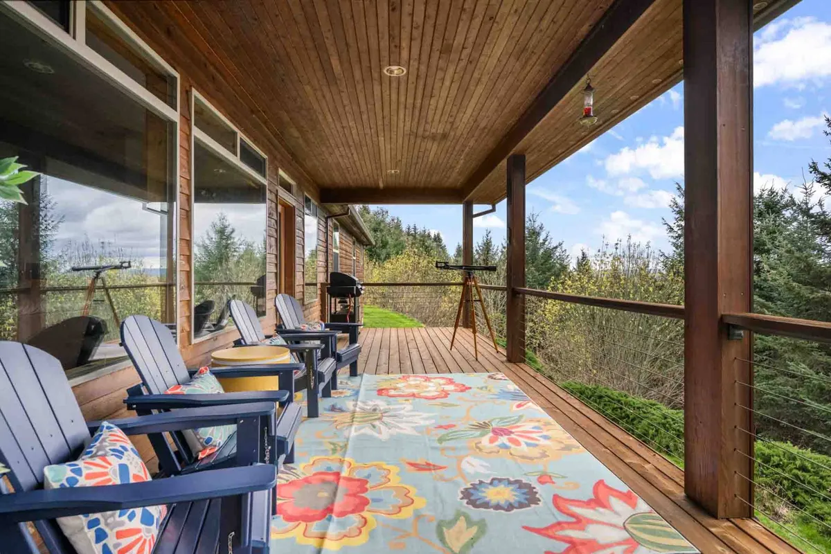 A spacious outdoor seating area with plush chairs and a vibrant rug, set against a backdrop of natural surroundings and a distant view of the landscape. The ambiance suggests a place for gatherings, storytelling, and enjoying food and drinks outdoors, with ample space for entertaining or quiet reflection.