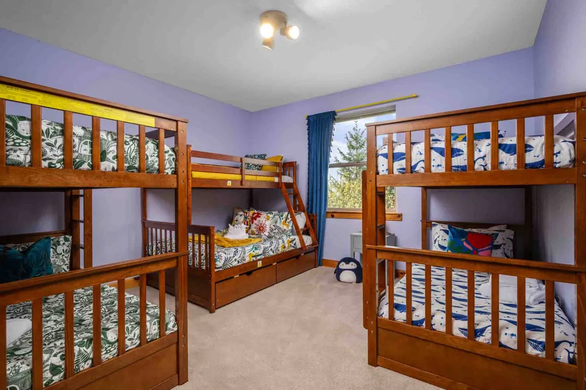 A playful and inviting bunk room featuring colorful bedding and a window with soft curtains. The space feels cheerful, with multiple bunks making it ideal for groups of kids or friends. There's plenty of light and the setup encourages both fun and restful nights.
