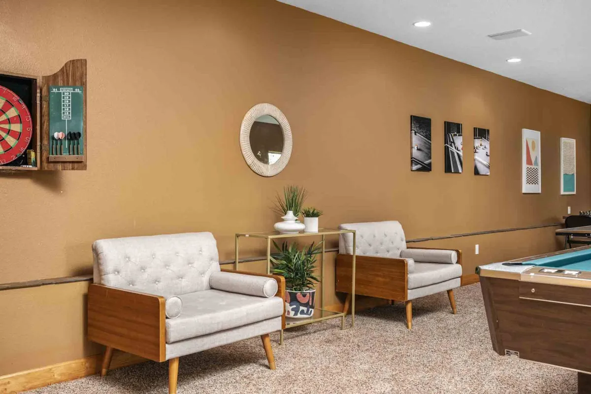 An inviting interior game room with a pool table, dartboard, stylish armchairs, and artwork, designed for casual, relaxed gatherings. The space is set up for friendly competition and socialization, supporting team-building and entertainment.