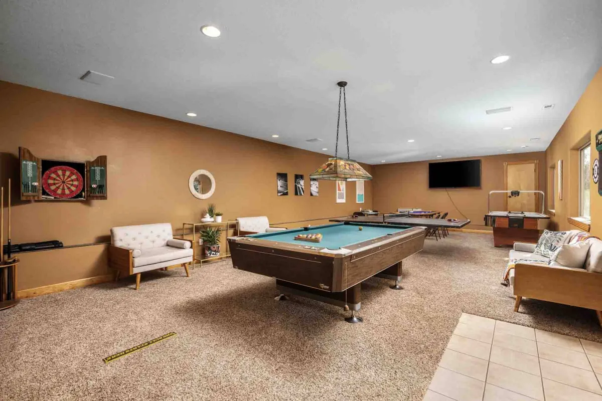 A vibrant game room featuring a pool table, dartboard, comfortable seating, and a television—set up for friendly competition and family fun. The room's layout invites lively tournaments and shared activities.