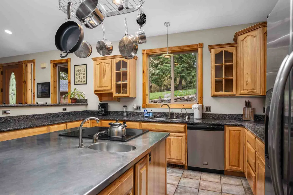 A gourmet kitchen highlighted by stainless steel appliances, granite countertops, a hanging pot rack, and a large window offering an inviting view. The space is set up for cooking, baking, and entertaining, reflecting quality and attention to detail.