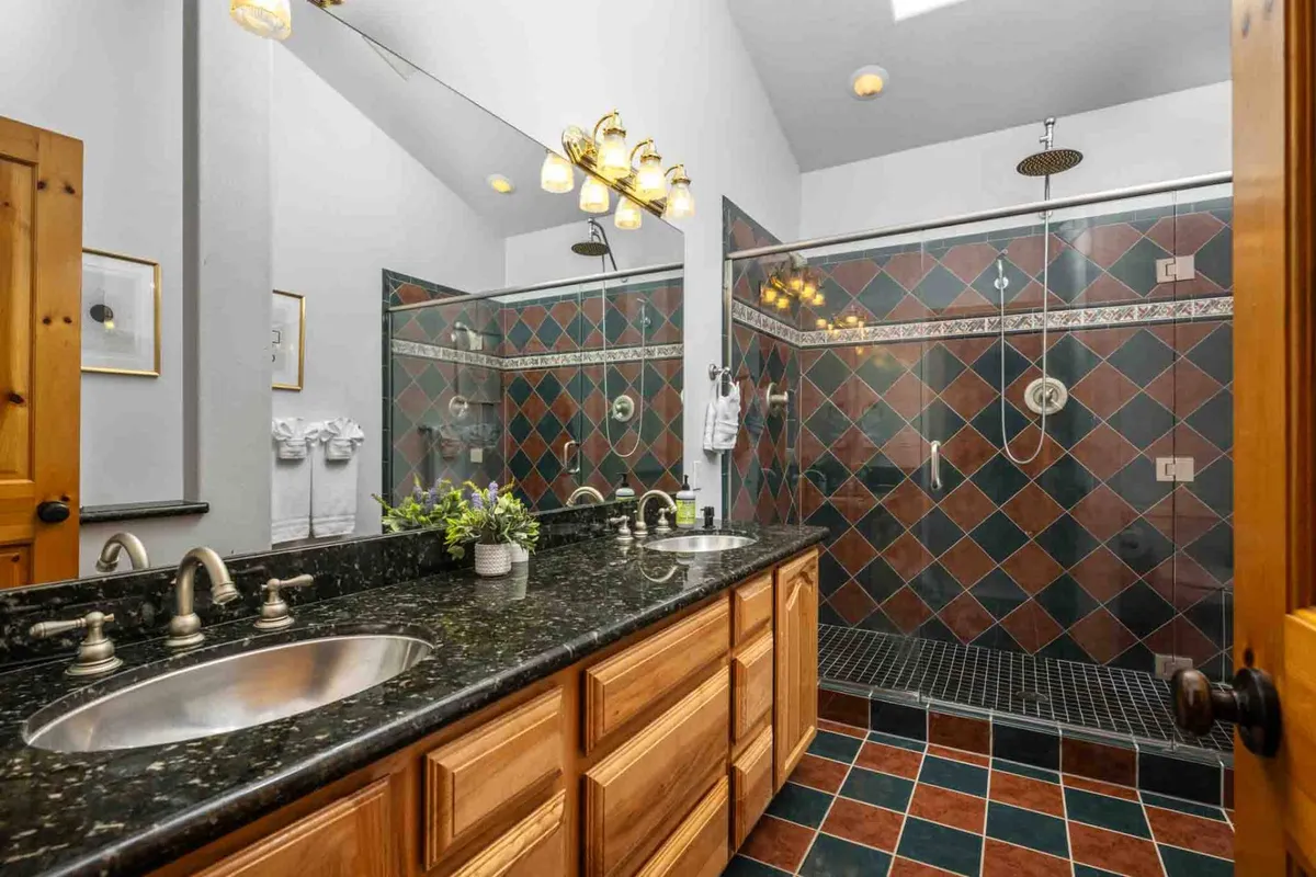 A modern bathroom with double sinks, sleek fixtures, a spacious walk-in shower, and vibrant tiled walls. The room is filled with natural light, creating a calming and rejuvenating ambiance ideal for self-care routines.